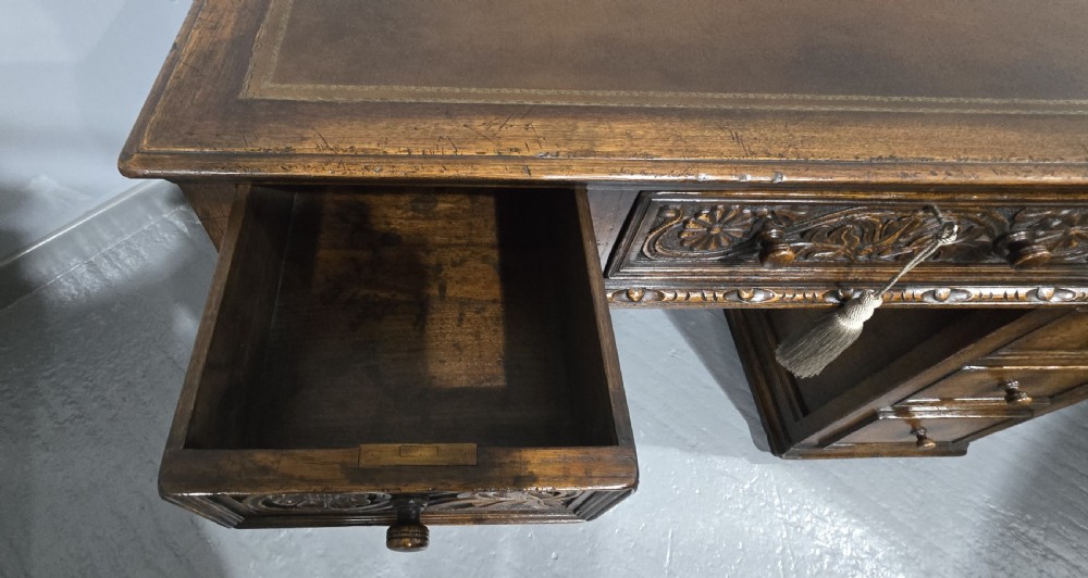 An antique dark oak pedestal desk featuring carved floral frieze drawers, turned wooden knobs, and two pedestals with three drawers each. View IV