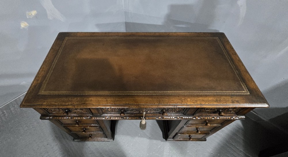 An antique dark oak pedestal desk featuring carved floral frieze drawers, turned wooden knobs, and two pedestals with three drawers each. View VII