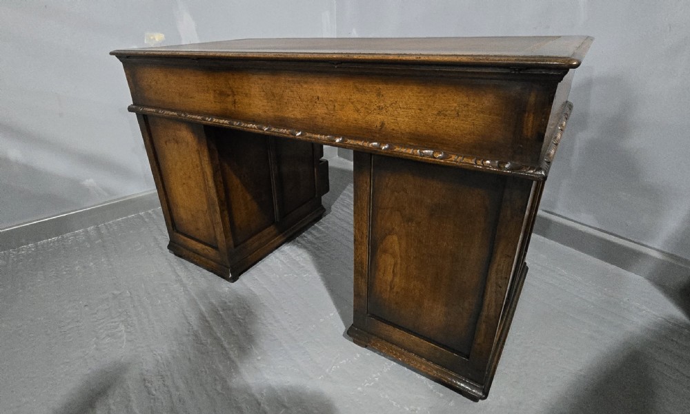 An antique dark oak pedestal desk featuring carved floral frieze drawers, turned wooden knobs, and two pedestals with three drawers each. View X