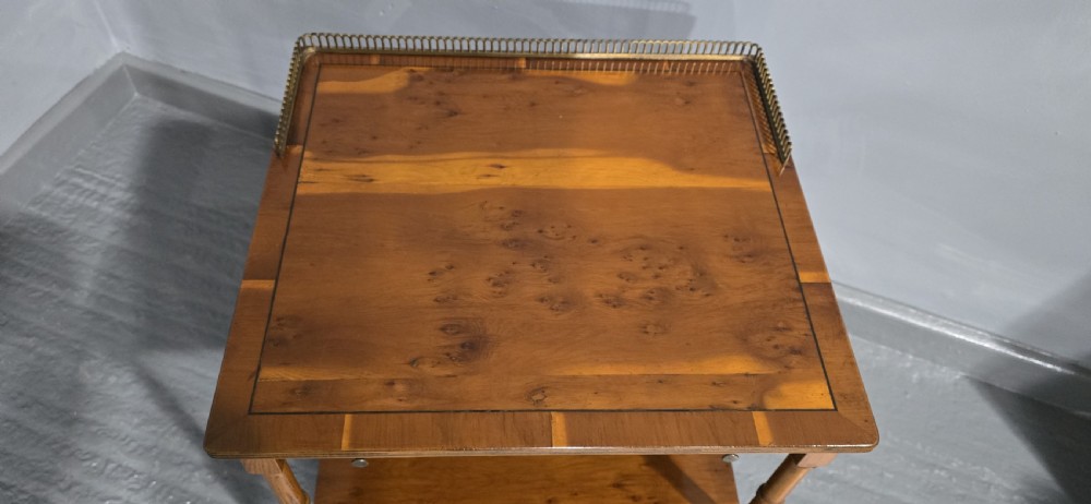 A two-tiered yew wood lamp table featuring a brass gallery top rail, turned legs, a lower drawer, and brass castors. View IV