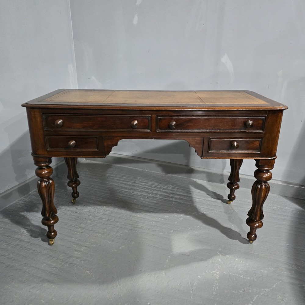 A William IV freestanding mahogany desk featuring a leather writing surface, five drawers with wooden knob handles, and turned legs on brass castors.