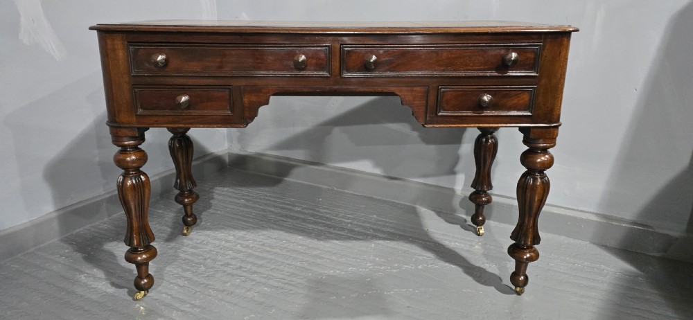 A William IV freestanding mahogany desk featuring a leather writing surface, five drawers with wooden knob handles, and turned legs on brass castors. View II