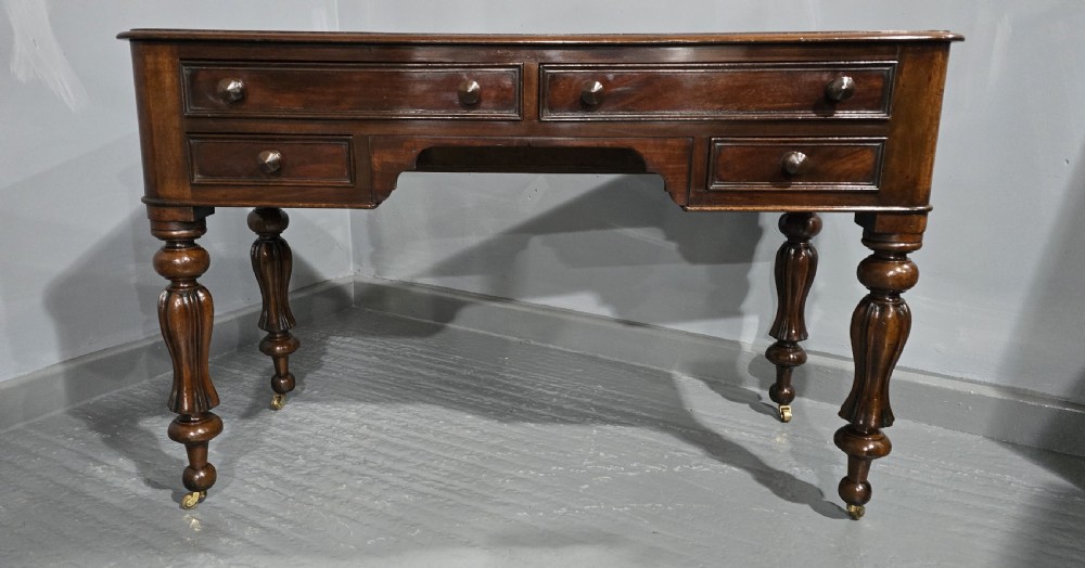 A William IV freestanding mahogany desk featuring a leather writing surface, five drawers with wooden knob handles, and turned legs on brass castors. View V