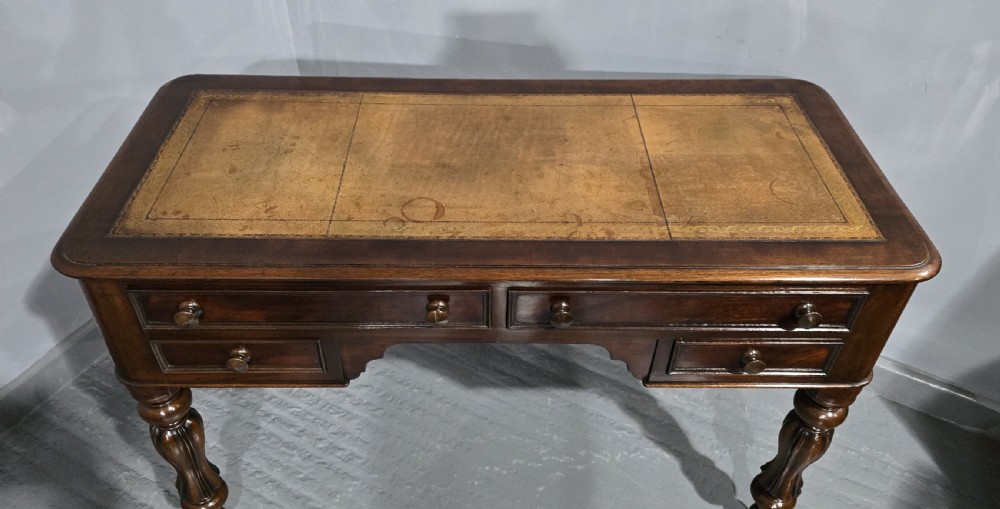 A William IV freestanding mahogany desk featuring a leather writing surface, five drawers with wooden knob handles, and turned legs on brass castors. View VII