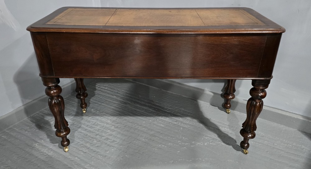 A William IV freestanding mahogany desk featuring a leather writing surface, five drawers with wooden knob handles, and turned legs on brass castors. View VIII