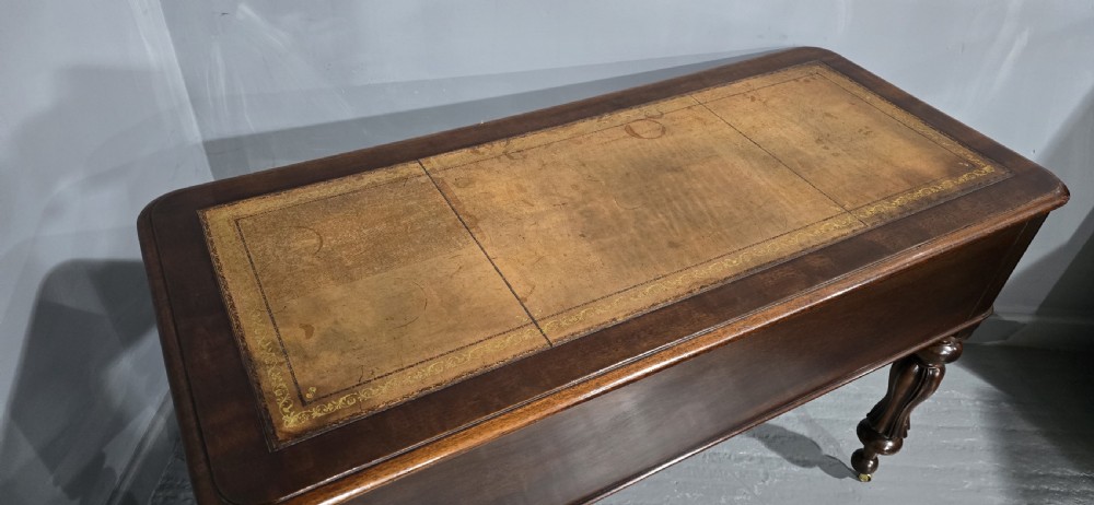 A William IV freestanding mahogany desk featuring a leather writing surface, five drawers with wooden knob handles, and turned legs on brass castors. View IX