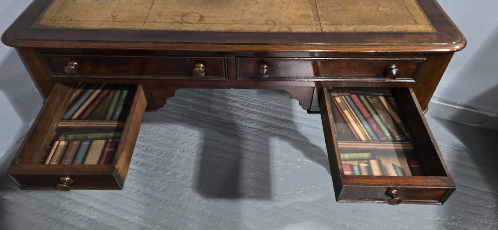 A William IV freestanding mahogany desk featuring a leather writing surface, five drawers with wooden knob handles, and turned legs on brass castors. View X