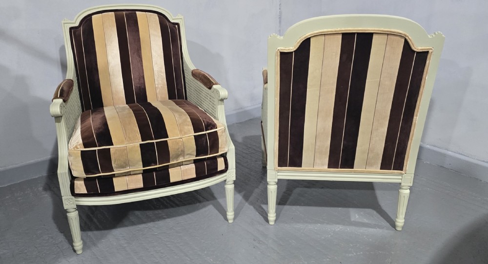 A pair of Louis XVI style French bergere armchairs featuring off-white painted wooden frames, caned sides, fluted legs, and striped brown velvet cushioned seats. View III