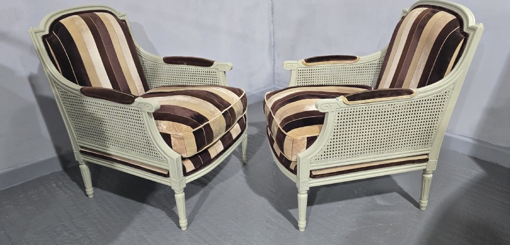 A pair of Louis XVI style French bergere armchairs featuring off-white painted wooden frames, caned sides, fluted legs, and striped brown velvet cushioned seats. View VII