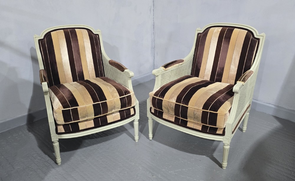 A pair of Louis XVI style French bergere armchairs featuring off-white painted wooden frames, caned sides, fluted legs, and striped brown velvet cushioned seats. View VIII