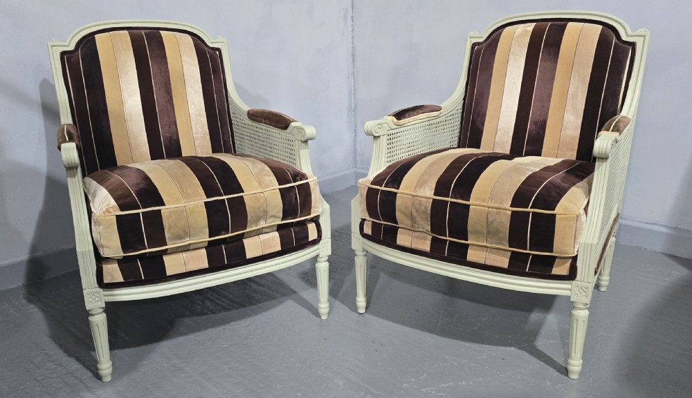 A pair of Louis XVI style French bergere armchairs featuring off-white painted wooden frames, caned sides, fluted legs, and striped brown velvet cushioned seats. View XI