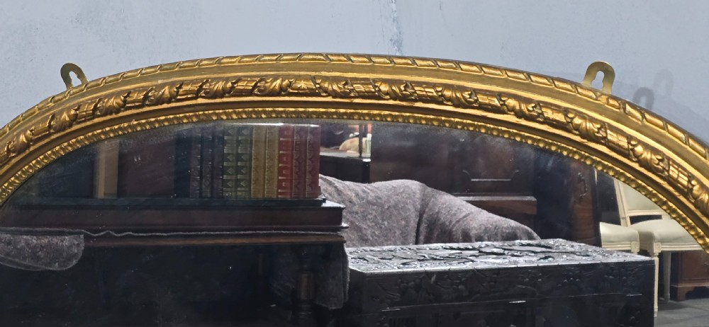 A Victorian arched overmantel mirror with an ornate gilded frame featuring detailed beaded moulding and a flat base. View V