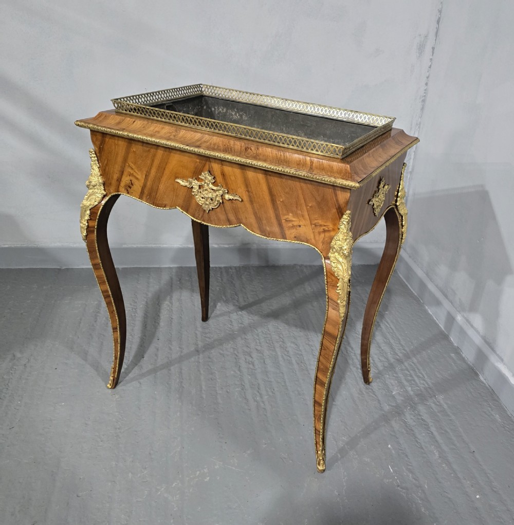 A Louis XV style satinwood jardiniere table featuring quartered wood veneer, ornate gilded bronze mounts, cabriole legs, a pierced brass gallery, and a metal liner.