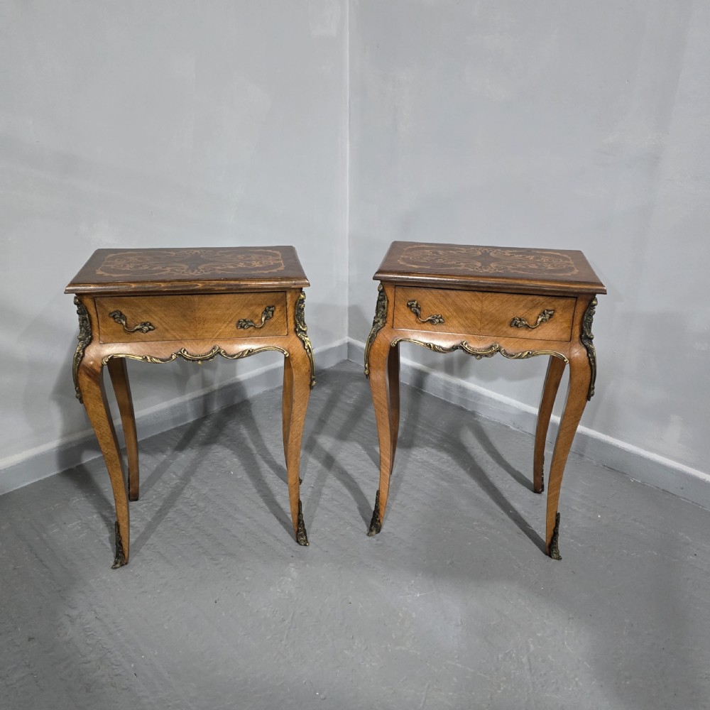 A pair of French Rococo style bedside tables with marquetry tops, single drawers, and ornate brass mounts on cabriole legs.
