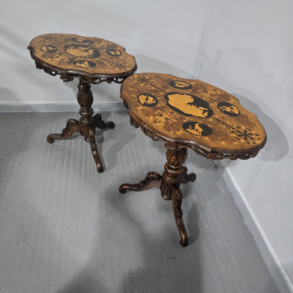 A pair of antique Black Forest carved walnut side tables featuring intricate marquetry tops with animal silhouettes on tripod pedestal bases.