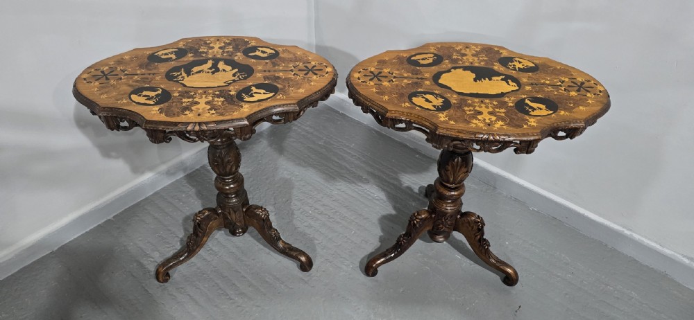 A pair of antique Black Forest carved walnut side tables featuring intricate marquetry tops with animal silhouettes on tripod pedestal bases. View X
