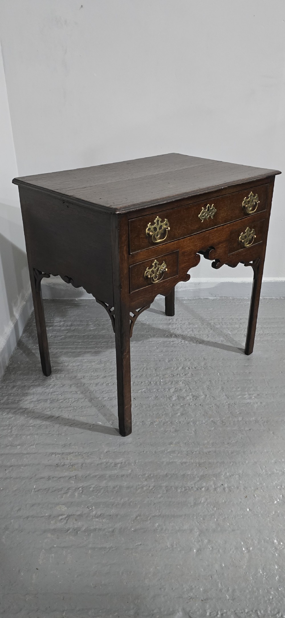 A dark oak 17th-century lowboy featuring three drawers with brass drop handles and a shaped kneehole apron set on straight square legs. View II