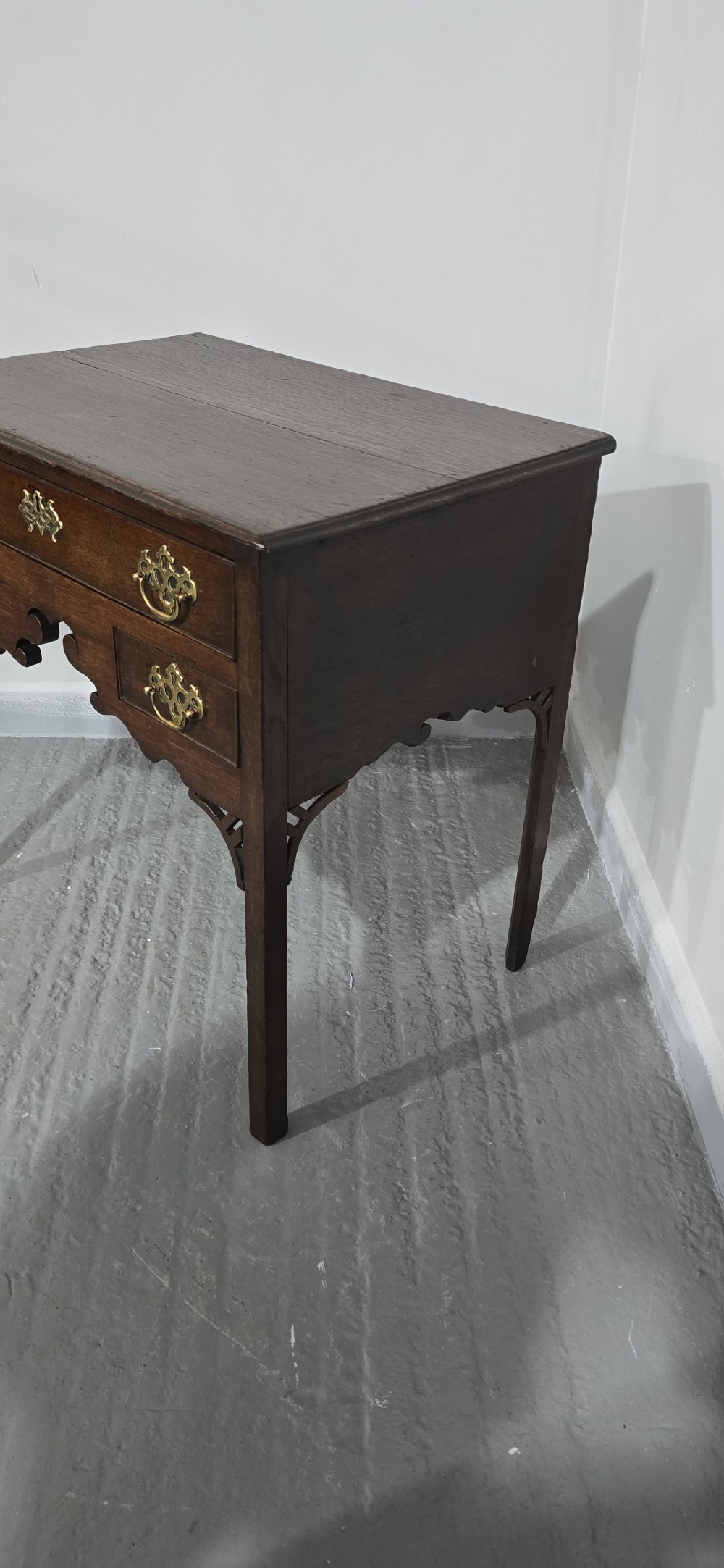 A dark oak 17th-century lowboy featuring three drawers with brass drop handles and a shaped kneehole apron set on straight square legs. View III