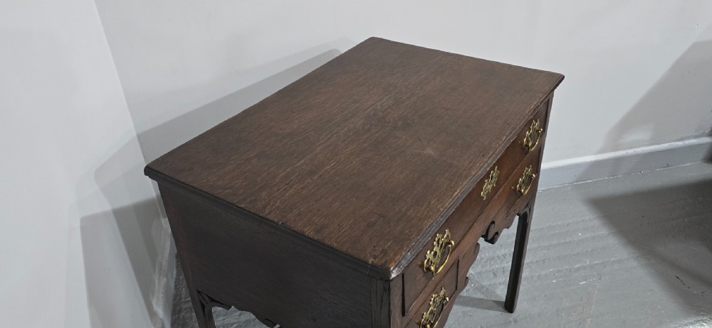 A dark oak 17th-century lowboy featuring three drawers with brass drop handles and a shaped kneehole apron set on straight square legs. View VII