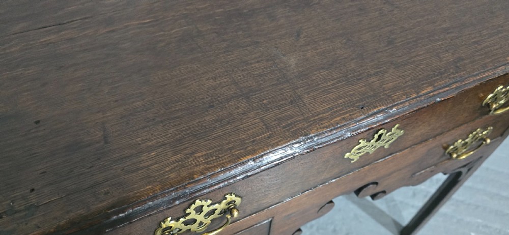 A dark oak 17th-century lowboy featuring three drawers with brass drop handles and a shaped kneehole apron set on straight square legs. View VIII