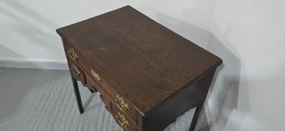 A dark oak 17th-century lowboy featuring three drawers with brass drop handles and a shaped kneehole apron set on straight square legs. View XII
