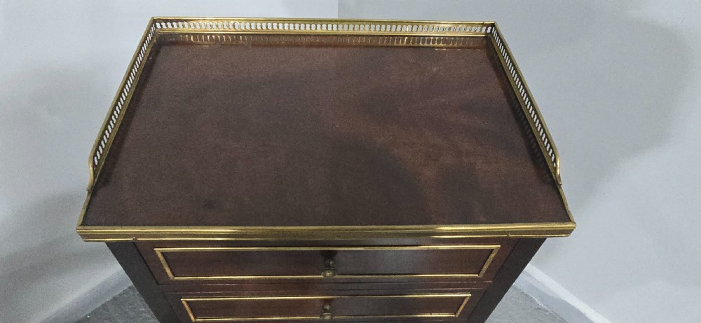 A tall, narrow dark mahogany chest of seven drawers with brass inlay banding, single knob handles, a brass gallery top, and turned tapered legs. View X