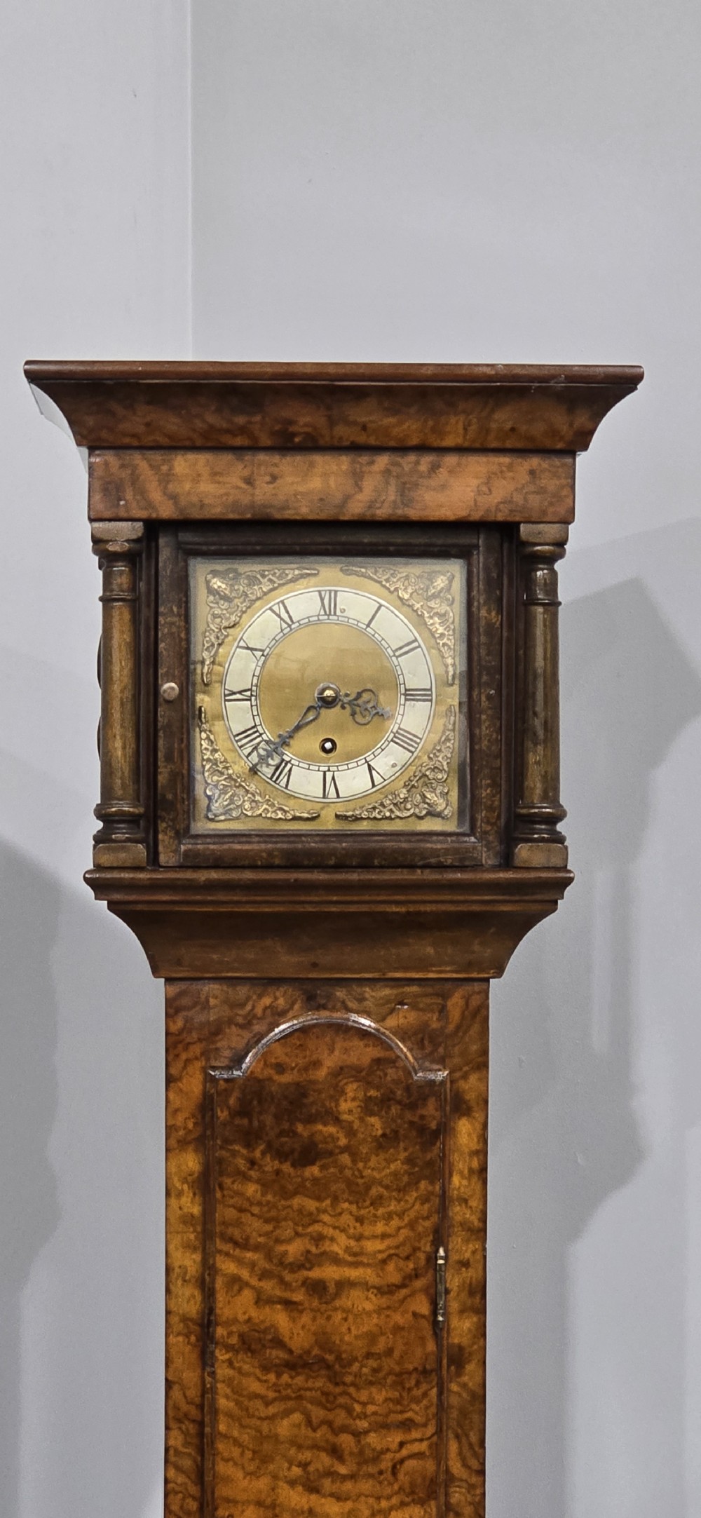 A slim floor-standing longcase clock crafted from figured burr walnut with a square brass dial and bracket feet. View IV