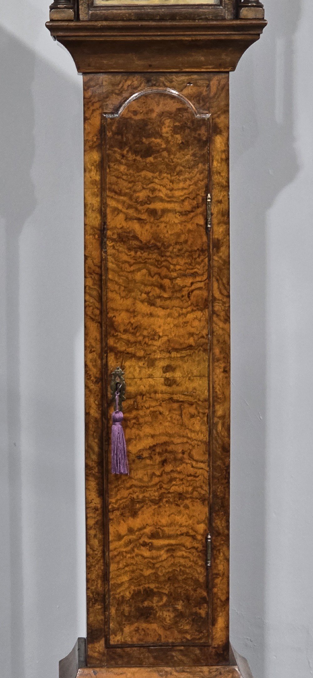 A slim floor-standing longcase clock crafted from figured burr walnut with a square brass dial and bracket feet. View V