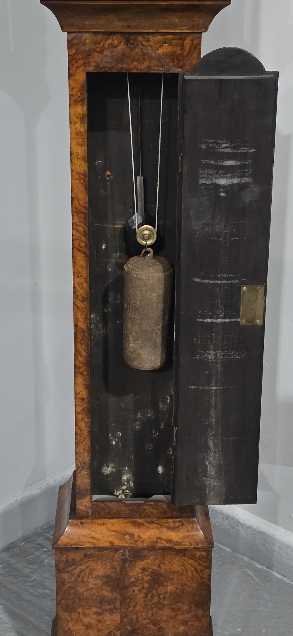A slim floor-standing longcase clock crafted from figured burr walnut with a square brass dial and bracket feet. View VII