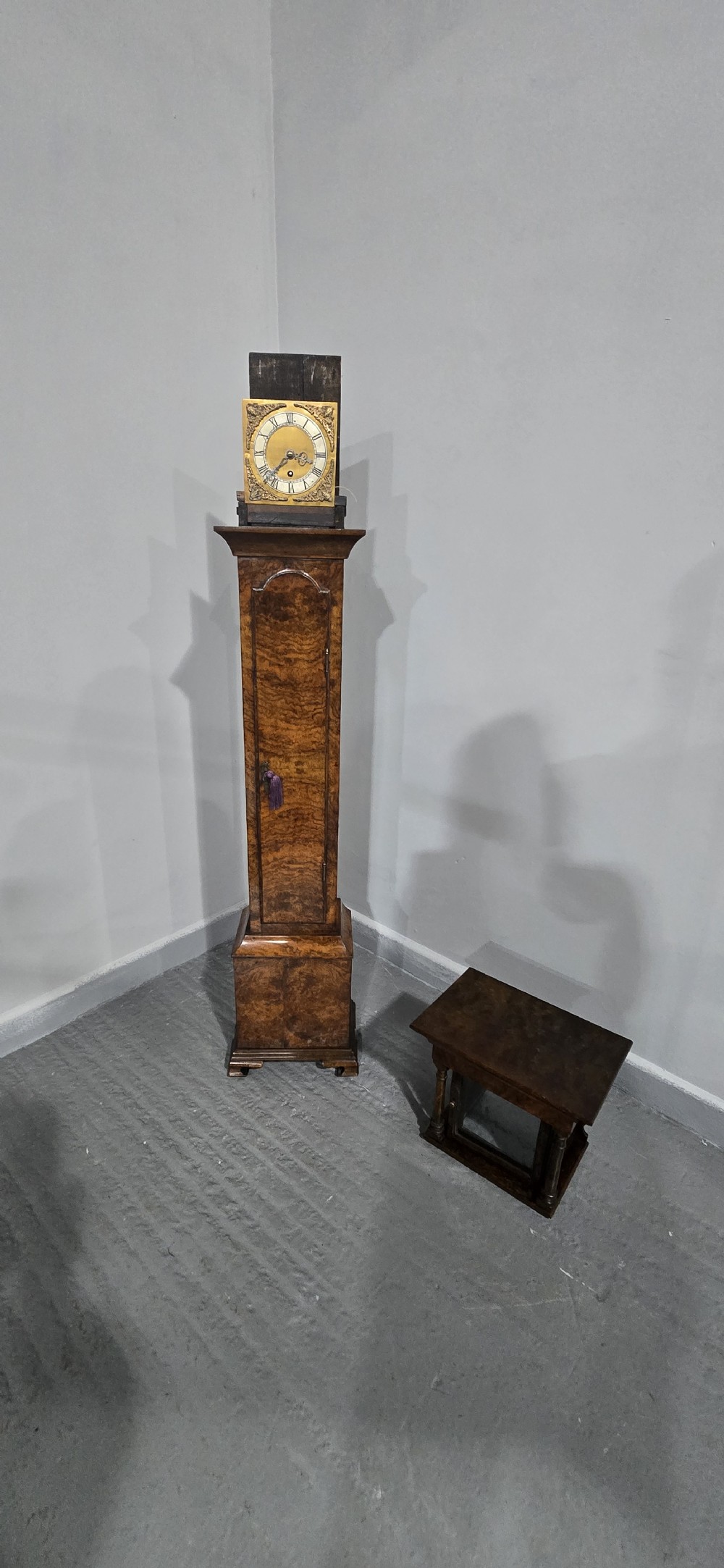 A slim floor-standing longcase clock crafted from figured burr walnut with a square brass dial and bracket feet. View VIII