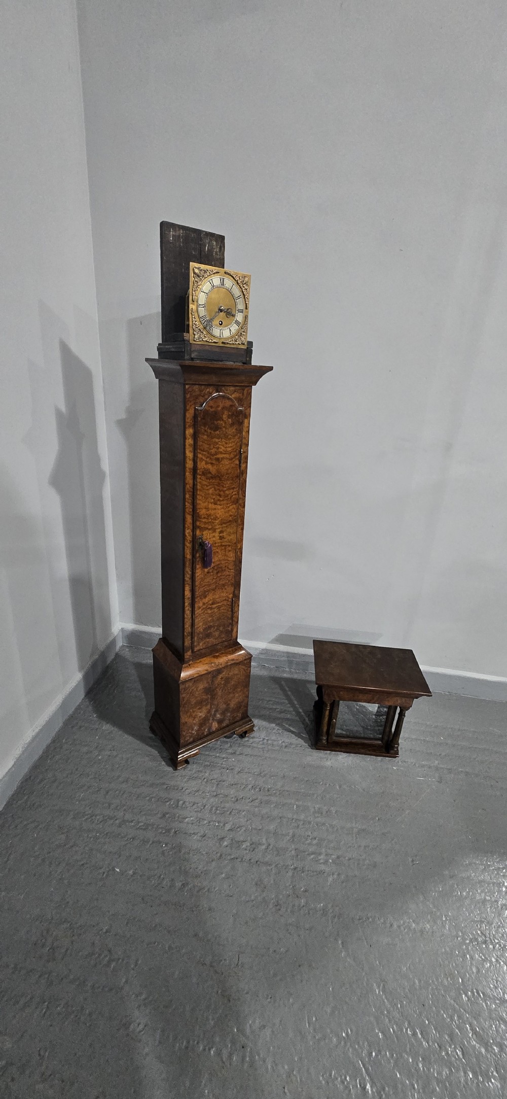 A slim floor-standing longcase clock crafted from figured burr walnut with a square brass dial and bracket feet. View XIII