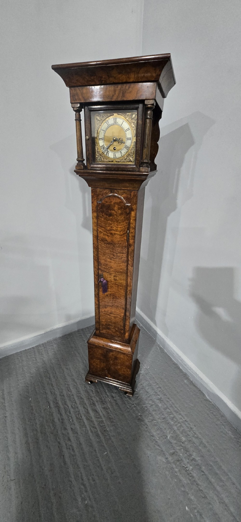 A slim floor-standing longcase clock crafted from figured burr walnut with a square brass dial and bracket feet. View XVI