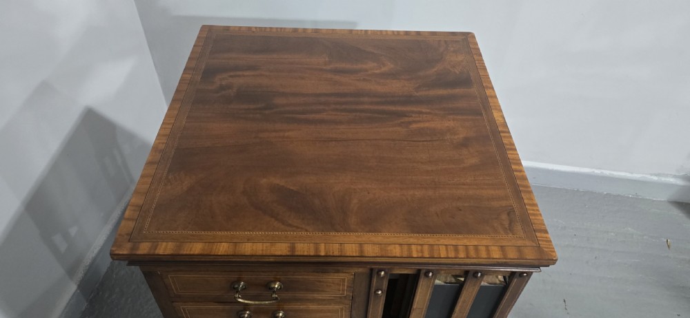 An Edwardian inlaid mahogany revolving bookcase featuring three small side drawers with brass drop handles, vertical timber slats, and metal castors on the base. View II
