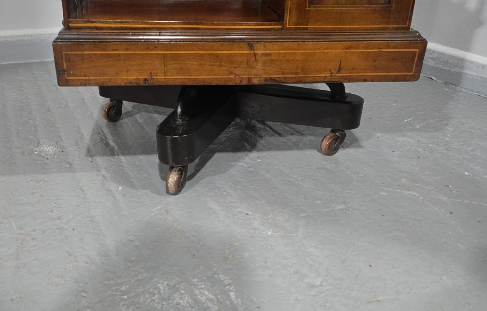 An Edwardian inlaid mahogany revolving bookcase featuring three small side drawers with brass drop handles, vertical timber slats, and metal castors on the base. View XIV