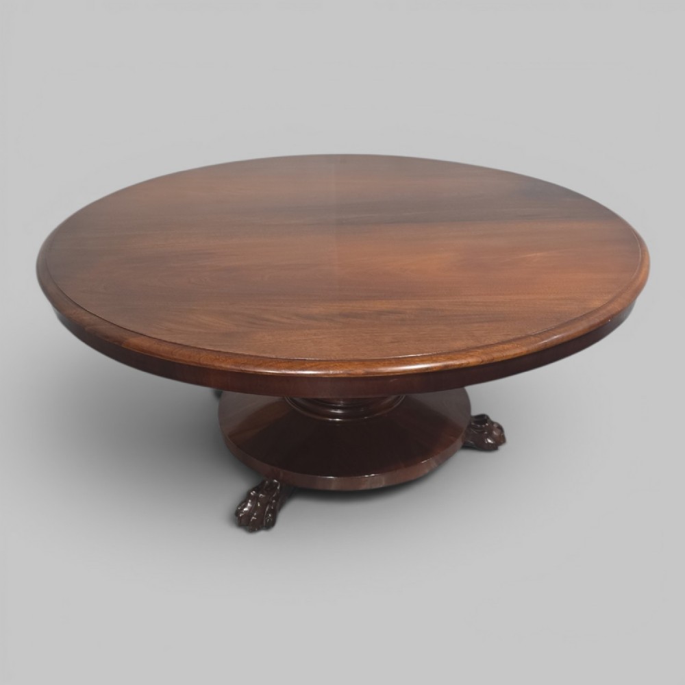 A low, circular mahogany coffee table featuring a smooth polished top supported by a central turned pedestal with carved claw feet.
