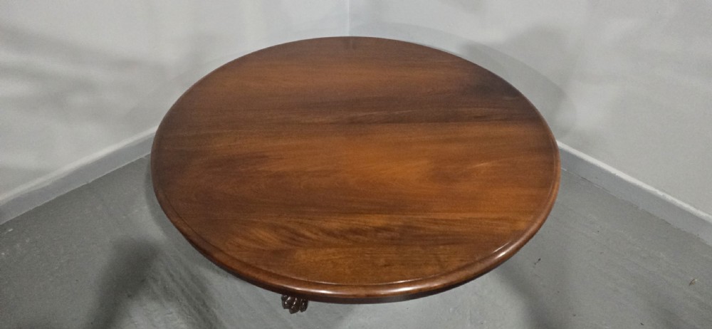 A low, circular mahogany coffee table featuring a smooth polished top supported by a central turned pedestal with carved claw feet. View III
