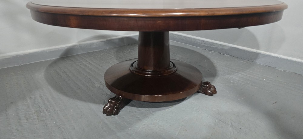 A low, circular mahogany coffee table featuring a smooth polished top supported by a central turned pedestal with carved claw feet. View IV