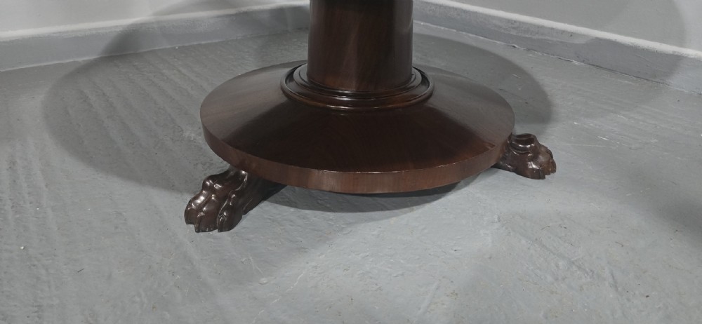A low, circular mahogany coffee table featuring a smooth polished top supported by a central turned pedestal with carved claw feet. View V