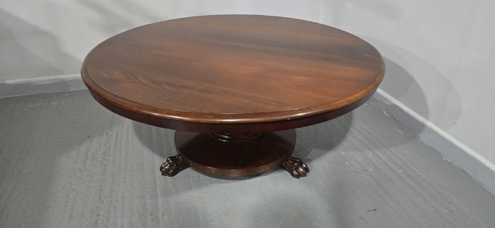 A low, circular mahogany coffee table featuring a smooth polished top supported by a central turned pedestal with carved claw feet. View IX