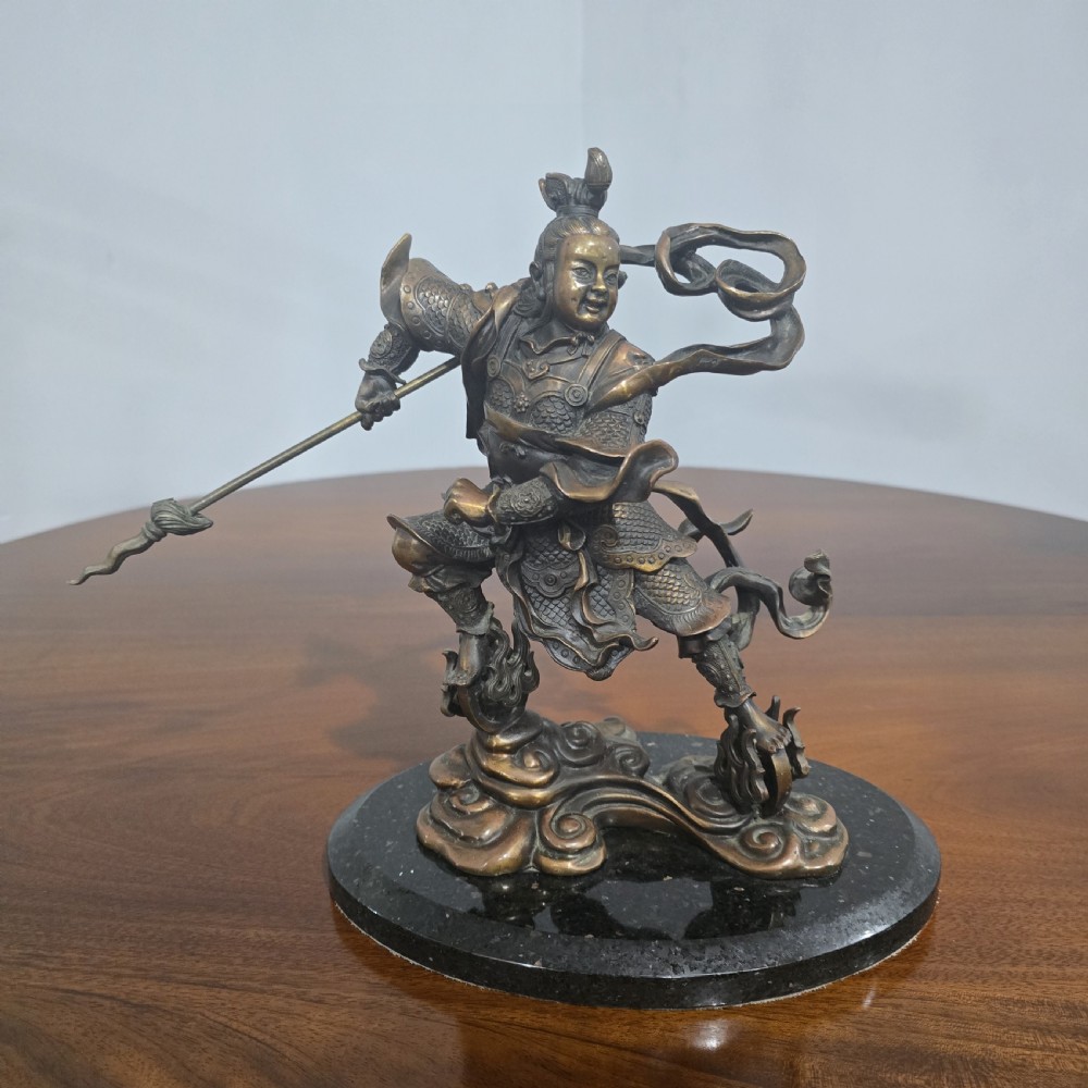 A detailed bronze sculpture depicting the Chinese mythological figure Ne Zha holding a spear, mounted on a circular black marble base. View II