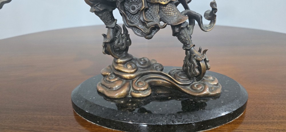 A detailed bronze sculpture depicting the Chinese mythological figure Ne Zha holding a spear, mounted on a circular black marble base. View V