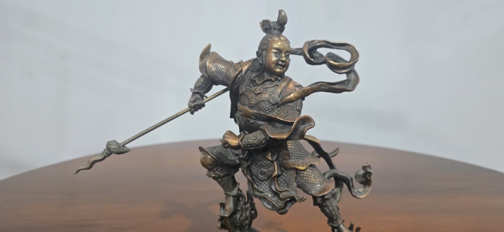 A detailed bronze sculpture depicting the Chinese mythological figure Ne Zha holding a spear, mounted on a circular black marble base. View VI