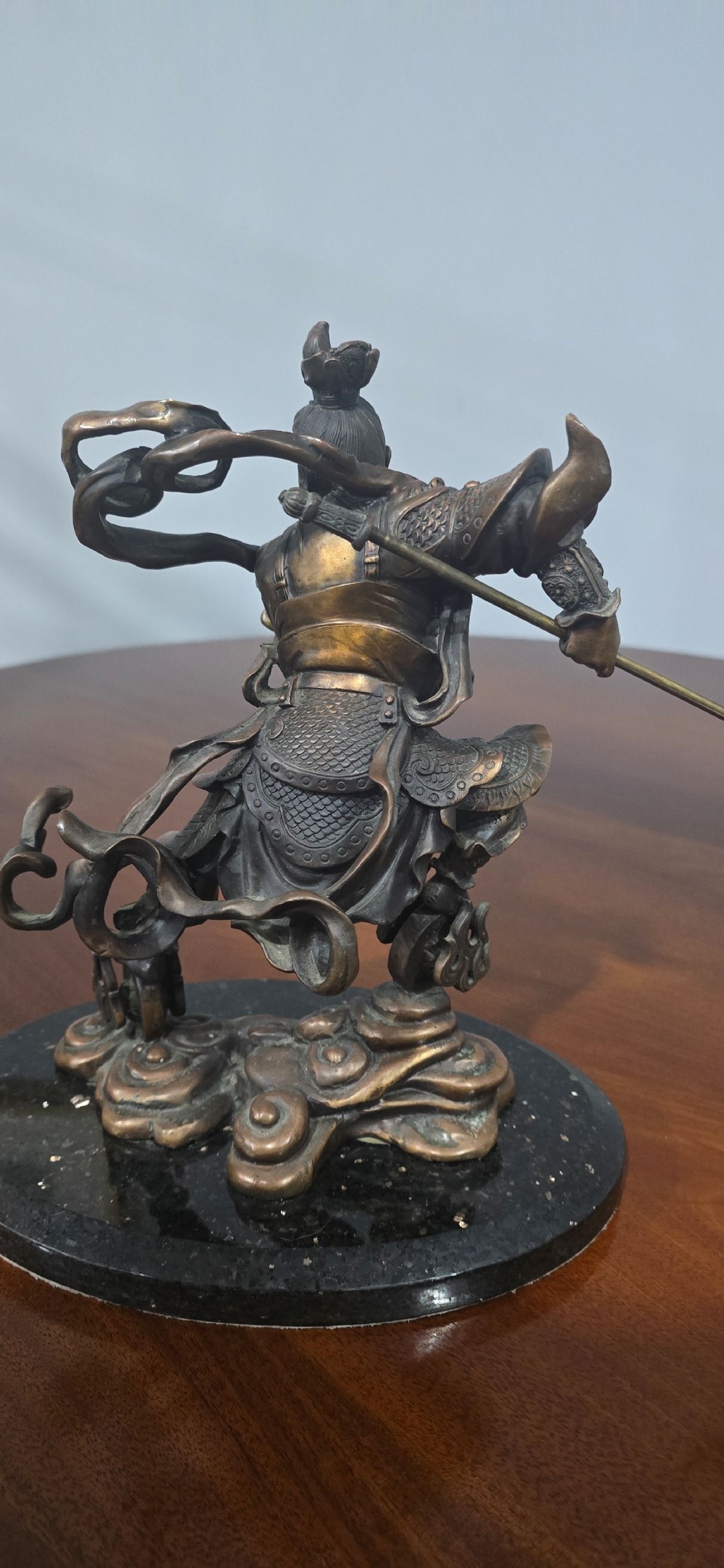 A detailed bronze sculpture depicting the Chinese mythological figure Ne Zha holding a spear, mounted on a circular black marble base. View IX