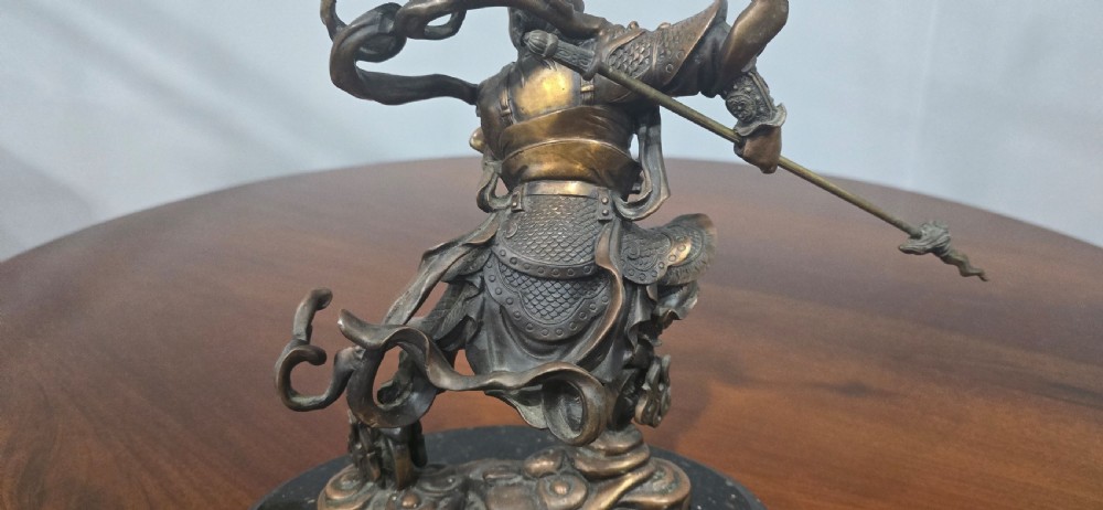 A detailed bronze sculpture depicting the Chinese mythological figure Ne Zha holding a spear, mounted on a circular black marble base. View XI