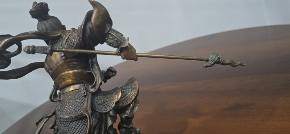 A detailed bronze sculpture depicting the Chinese mythological figure Ne Zha holding a spear, mounted on a circular black marble base. View XII