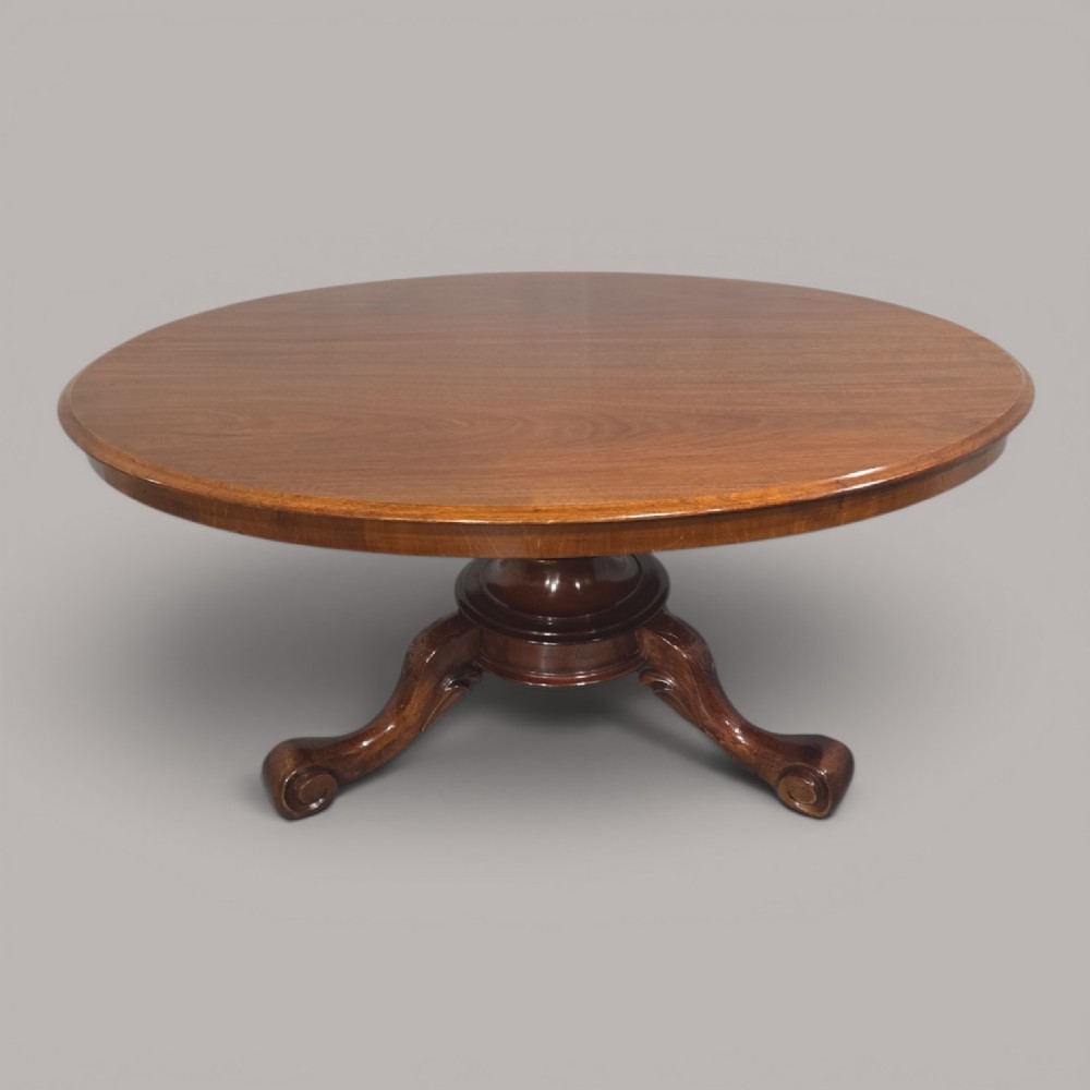 An oval mahogany coffee table featuring a polished surface, a central turned pedestal, and four carved cabriole legs terminating in scroll feet.