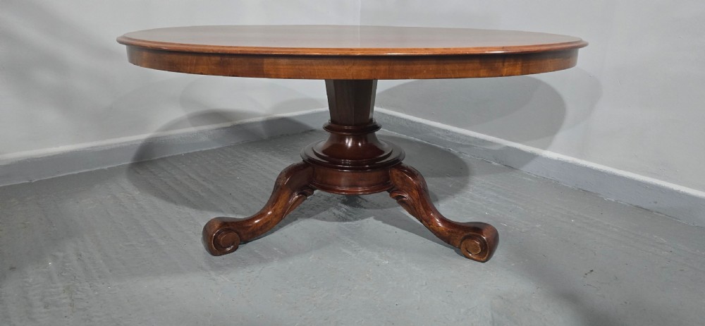 An oval mahogany coffee table featuring a polished surface, a central turned pedestal, and four carved cabriole legs terminating in scroll feet. View IV