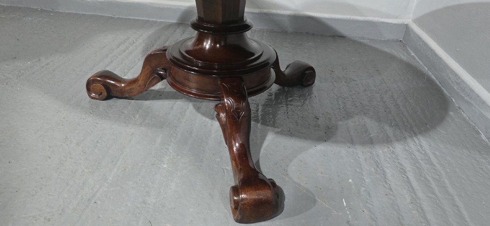 An oval mahogany coffee table featuring a polished surface, a central turned pedestal, and four carved cabriole legs terminating in scroll feet. View IX
