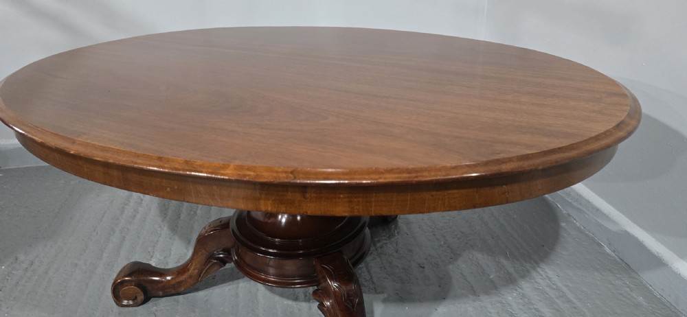 An oval mahogany coffee table featuring a polished surface, a central turned pedestal, and four carved cabriole legs terminating in scroll feet. View X