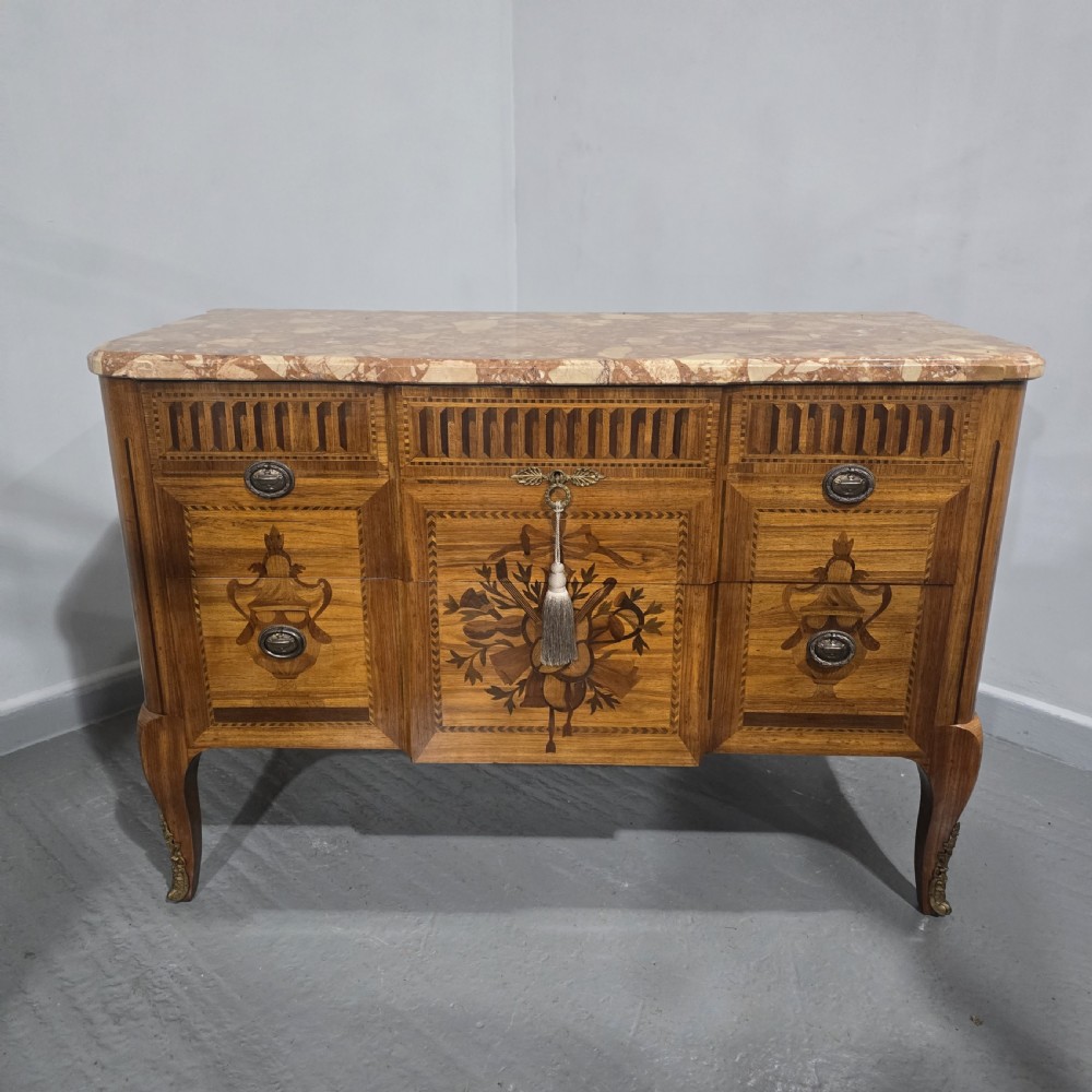 A French marquetry chest of drawers featuring inlaid urn and floral motifs, a contoured pink marble top, and cabriole legs. View II